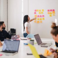 Bild Forschendes Lernen, mehrere Lernende in einen Raum mit Laptops und einer Person vor einem Whiteboard mit Post-It-Zetteln